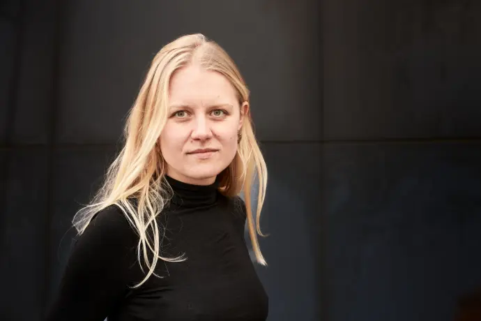 Helena Udsen, en kvinde med lang lyst hår, der står i sort trøje og kigger venligt ind i kameraet